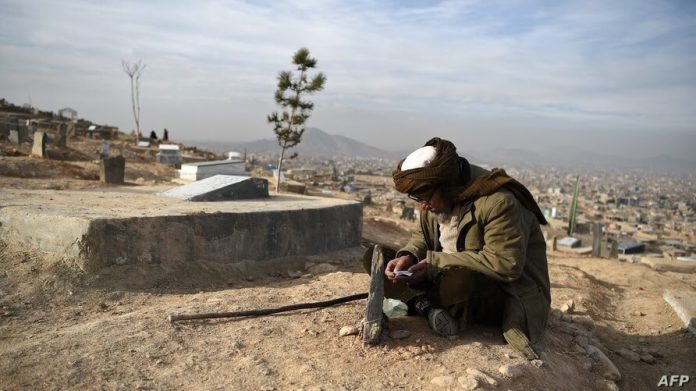 Un hombre lee el Corán junto a la tumba de un familiar en un cementerio en las afueras de Kabul, Afganistán, el 14 de enero de 2021.